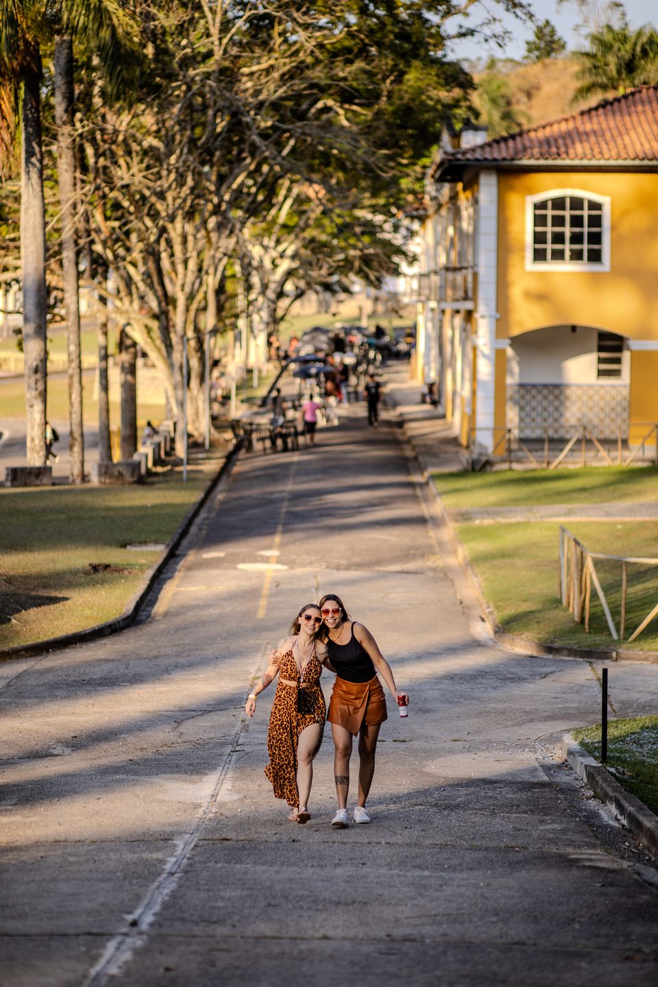 Duas visitantes caminhando pela alameda arborizada entre os casarões amarelos do espaço