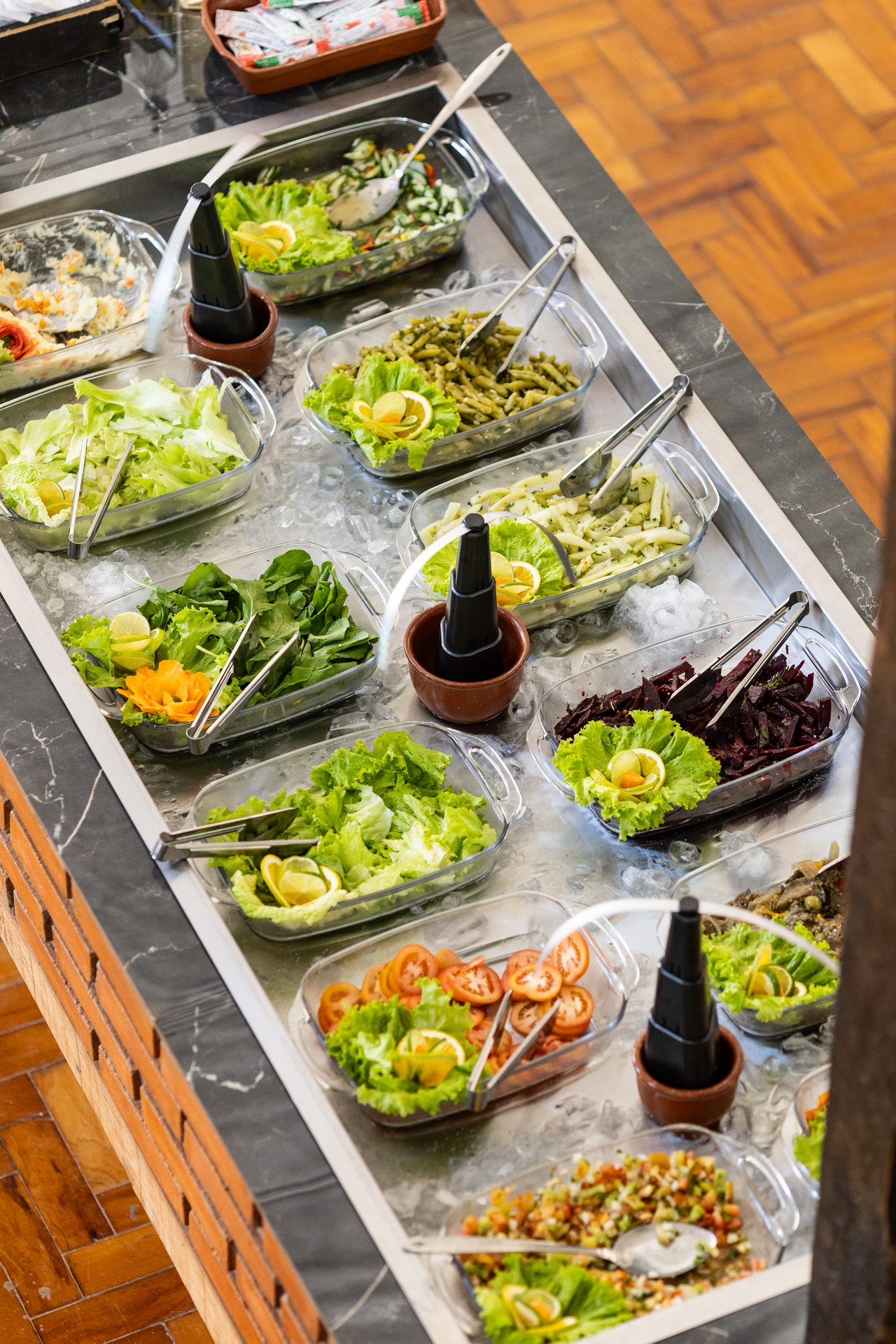 Balcão refrigerado do buffet com saladas, legumes e conservas em travessas de vidro