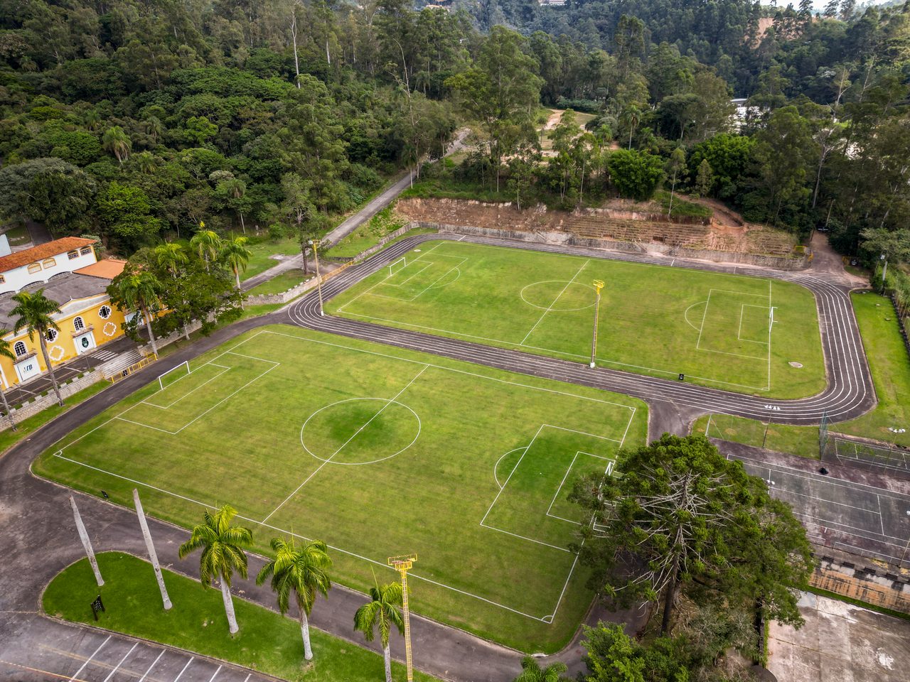 Vista aérea dos campos de futebol gramados do Instituto da Costela, cercados pela mata