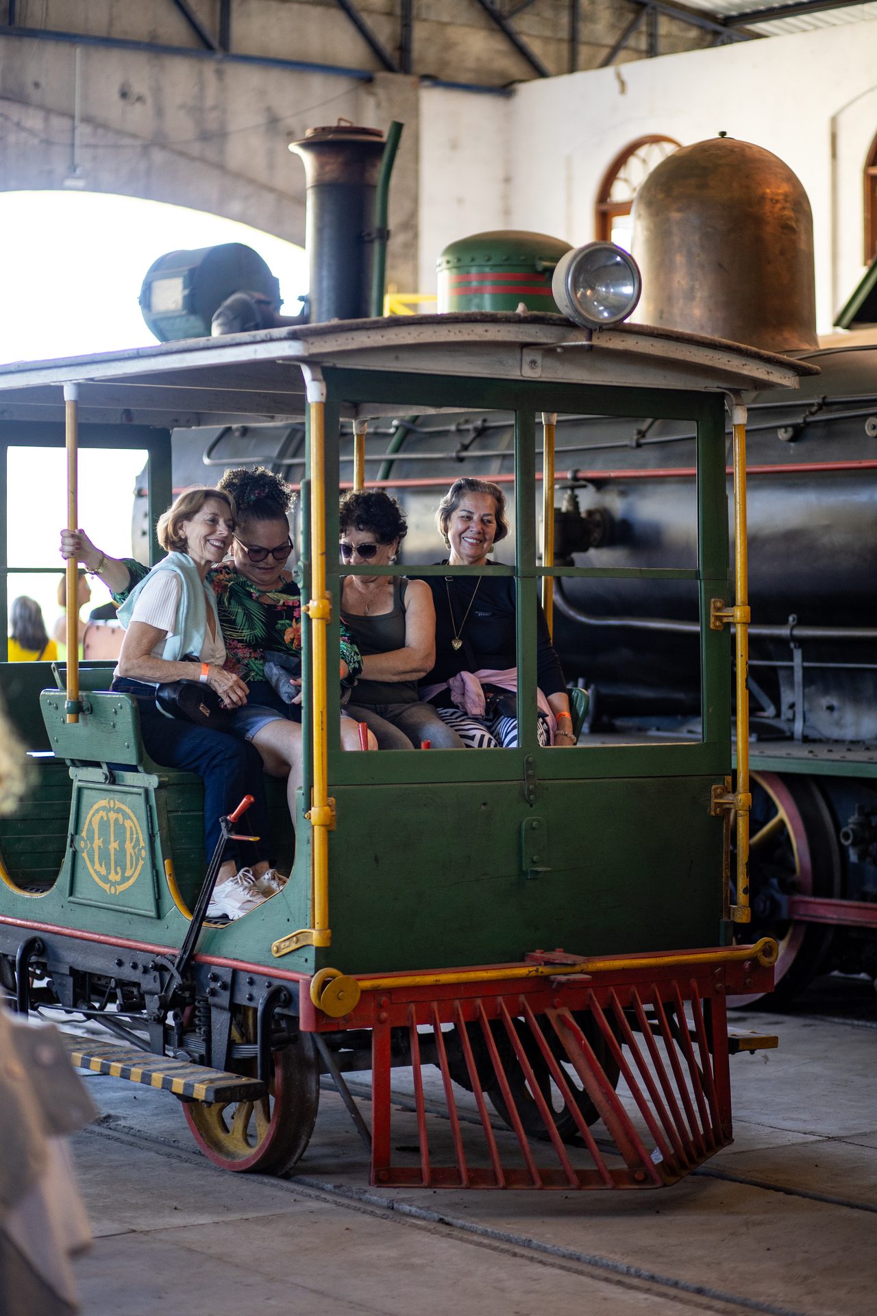 Visitantes sentados na cabine da locomotiva Maria Fumaça verde do acervo do museu