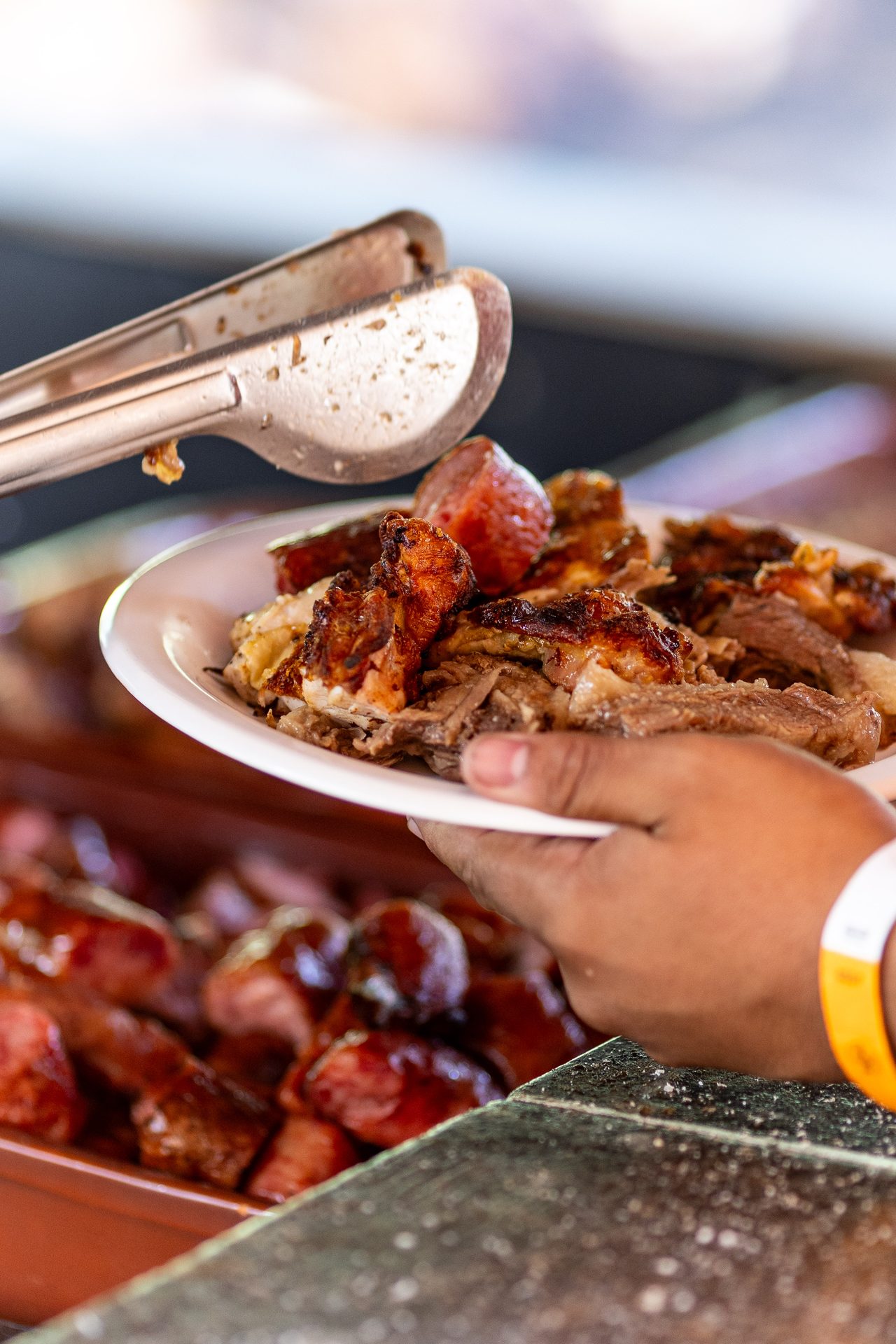 Prato branco sendo servido com carne desfiada da costela, ao lado da bandeja de linguiça