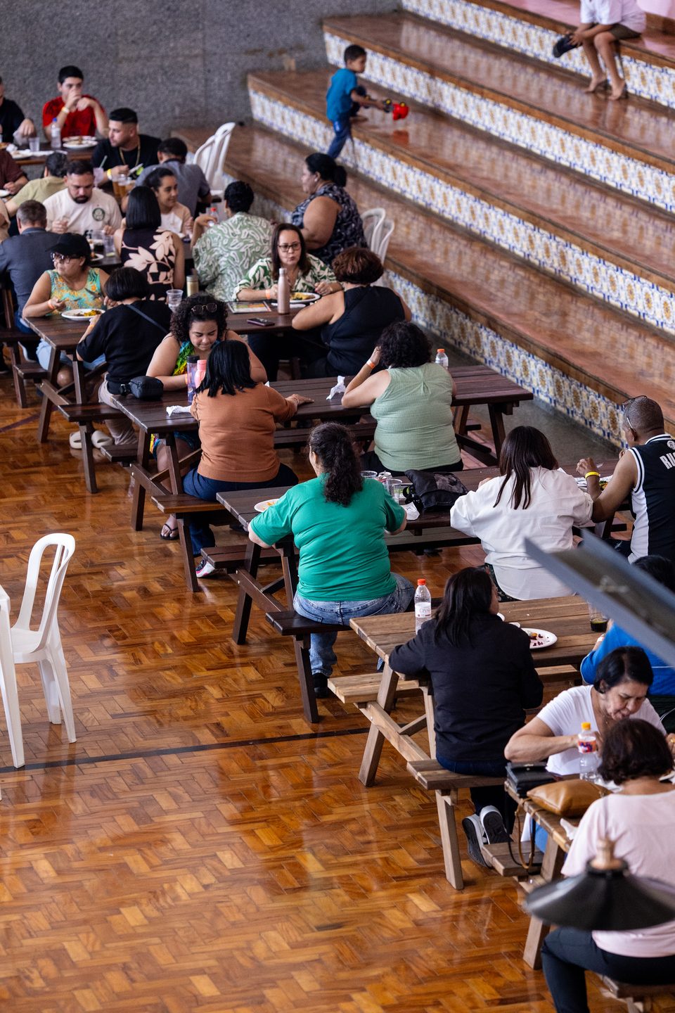 Famílias almoçando nas mesas da área coberta do restaurante, com as arquibancadas ao fundo